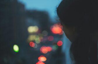 A young woman observing the noisy street at night from a window