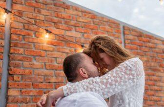 Loving couple millennials hug each other, touch forehead to forehead, resting on white bed.